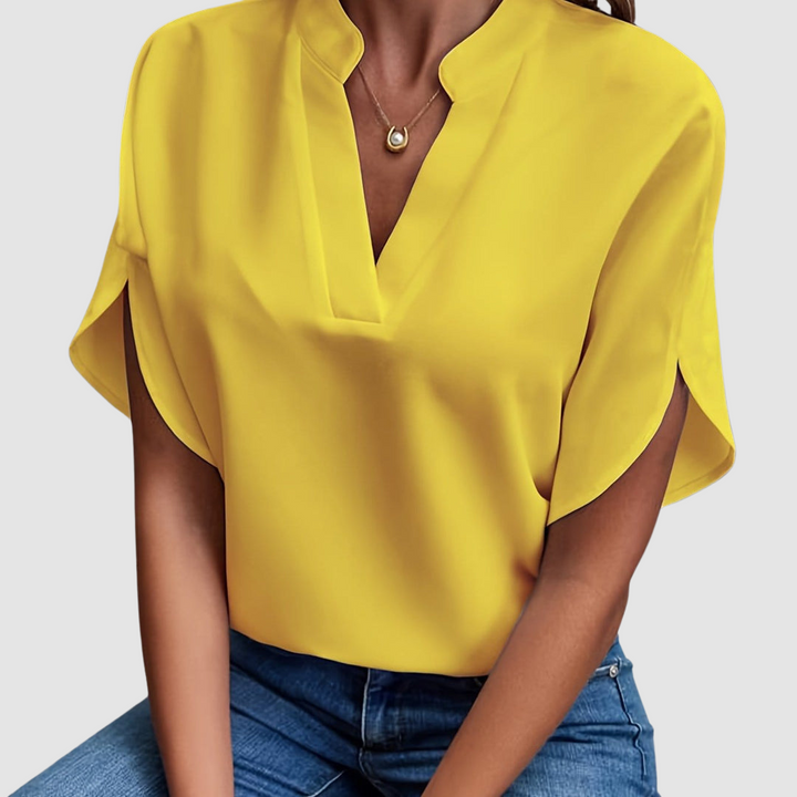 Yellow draped blouse with a sleek V-neck and flowing short sleeves, worn with blue jeans, in a neutral studio setting.