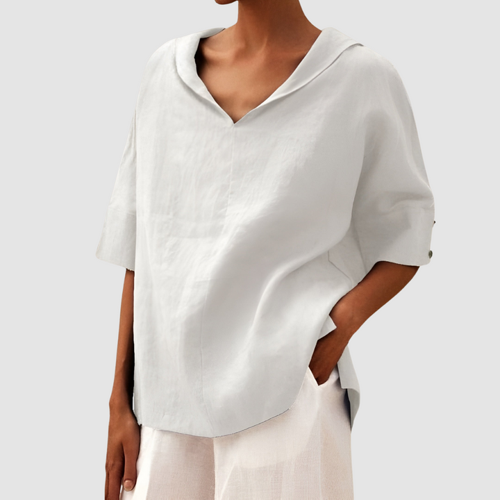 Light gray blouse with V-neck and short sleeves, worn with white pants, studio background.