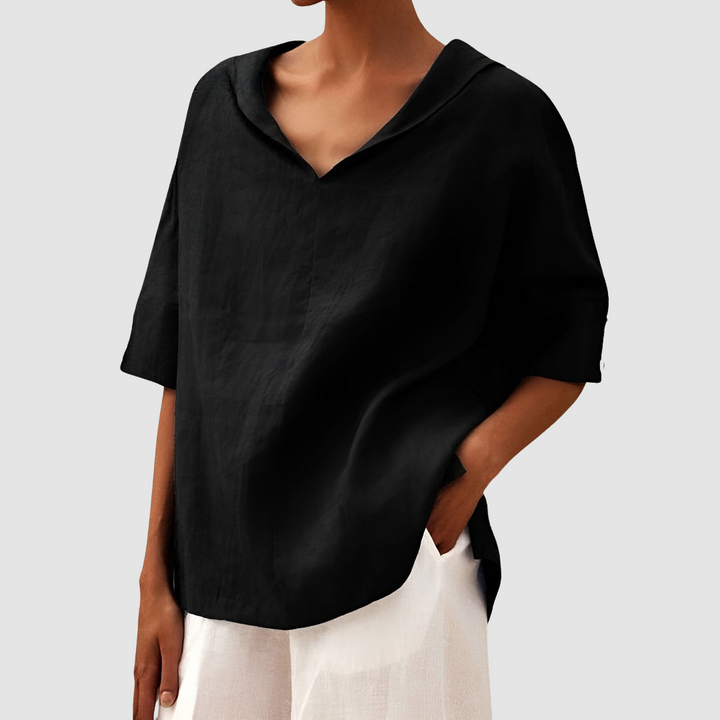 Black blouse with V-neck and short sleeves, styled with white pants, studio backdrop.