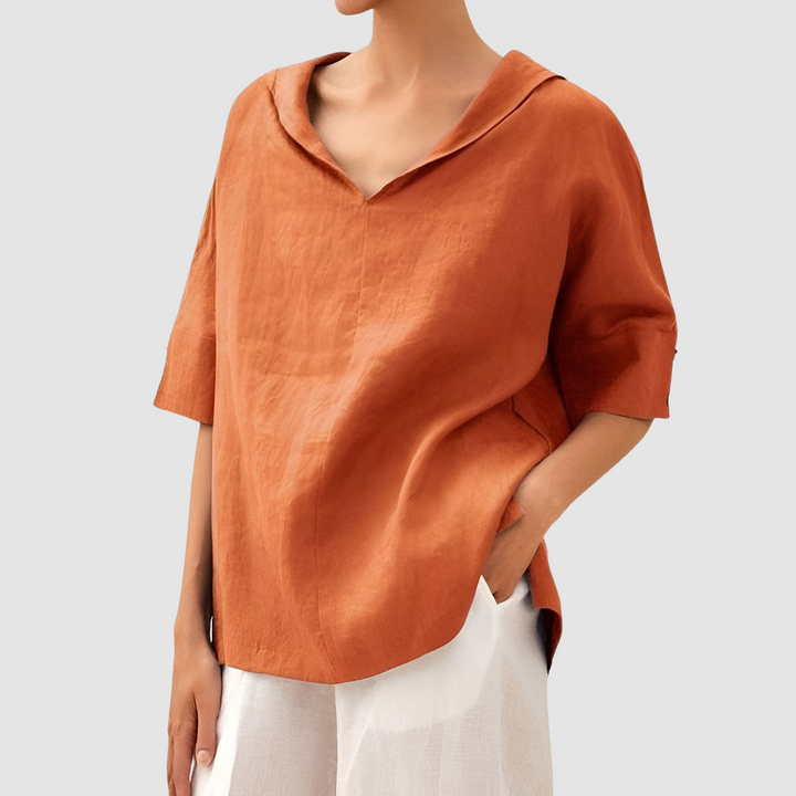 Orange blouse featuring a V-neck and short sleeves, worn with white pants, studio setting.