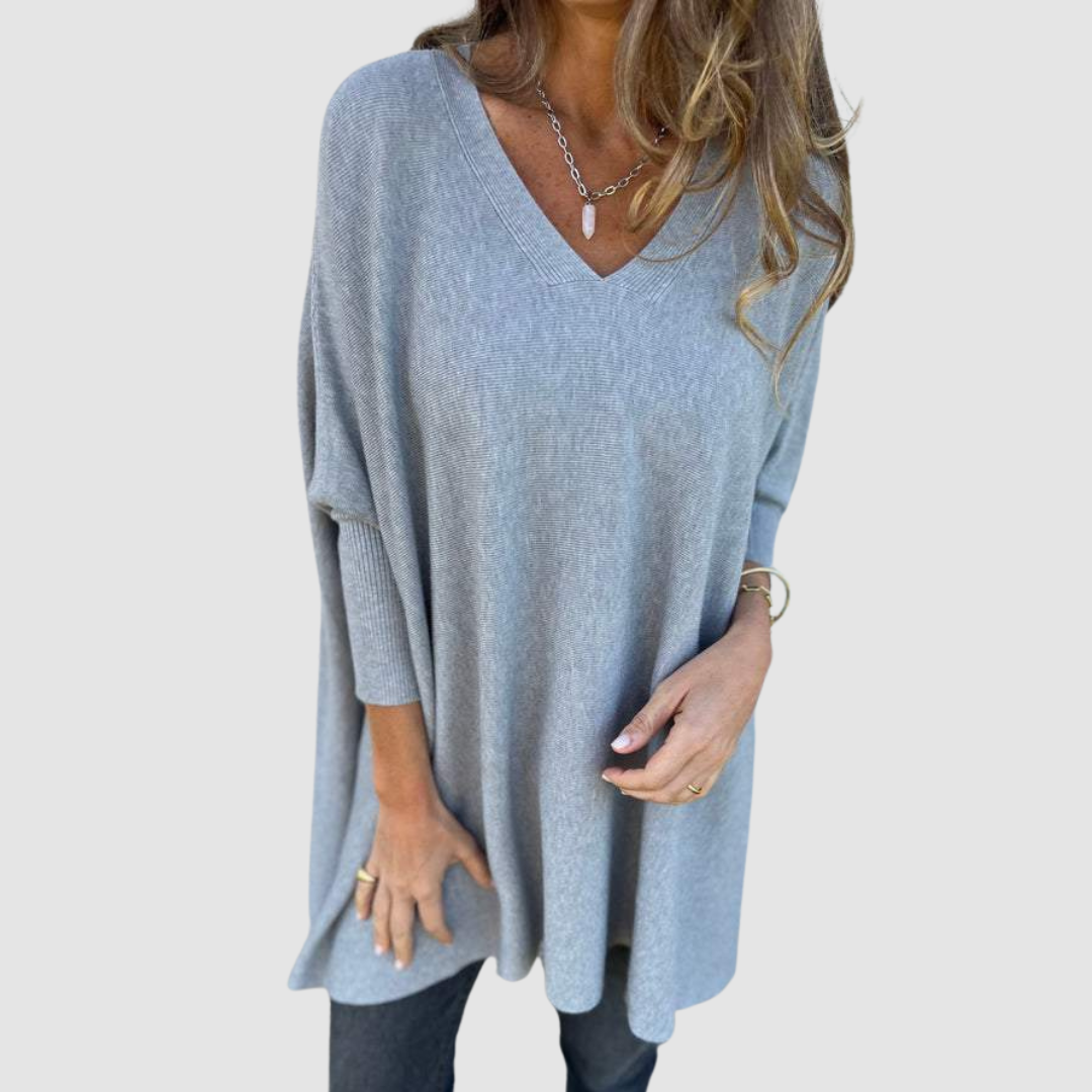 Gray v-neck sweater with long sleeves, worn by model with loose hair and jewelry on a plain background.