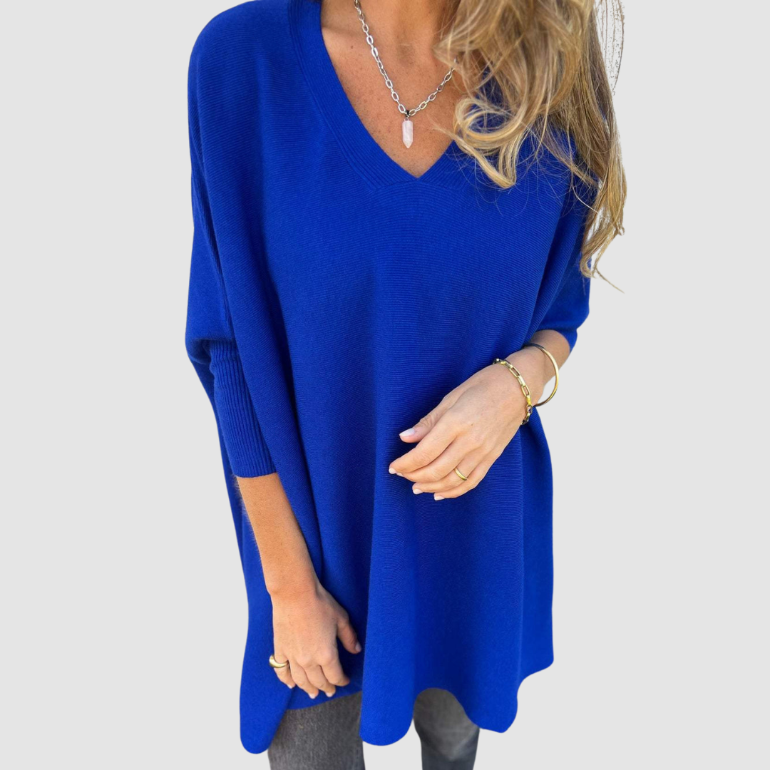 Blue v-neck sweater with long sleeves, worn by model with loose hair and jewelry on a plain background.