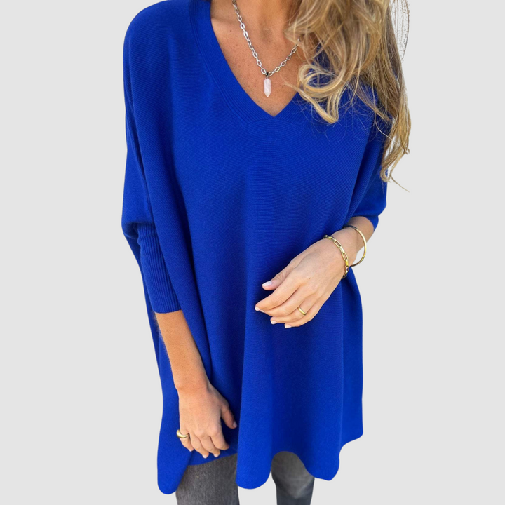 Blue v-neck sweater with long sleeves, worn by model with loose hair and jewelry on a plain background.