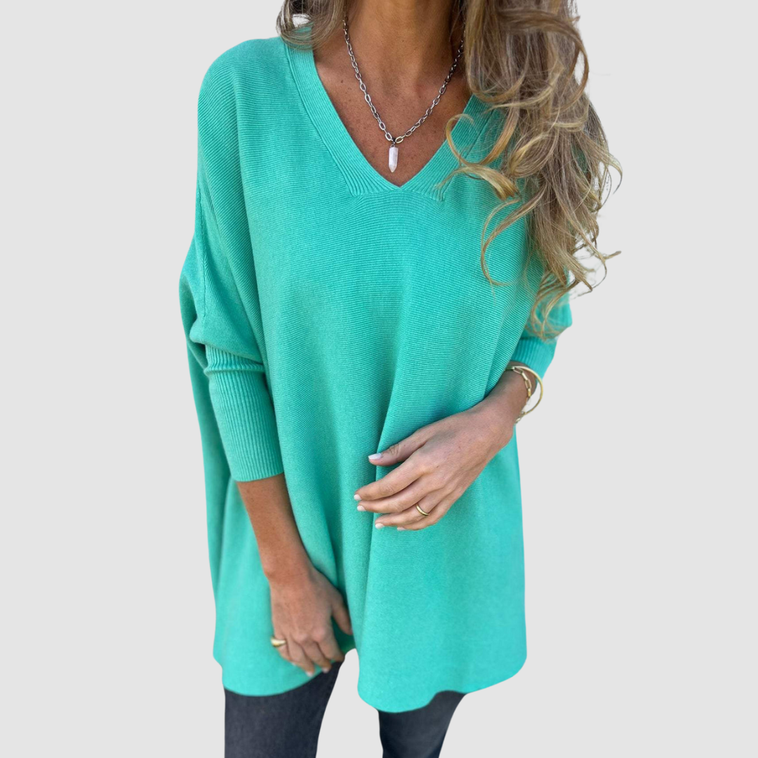 Teal v-neck sweater with long sleeves, worn by model with loose hair and jewelry on a plain background.