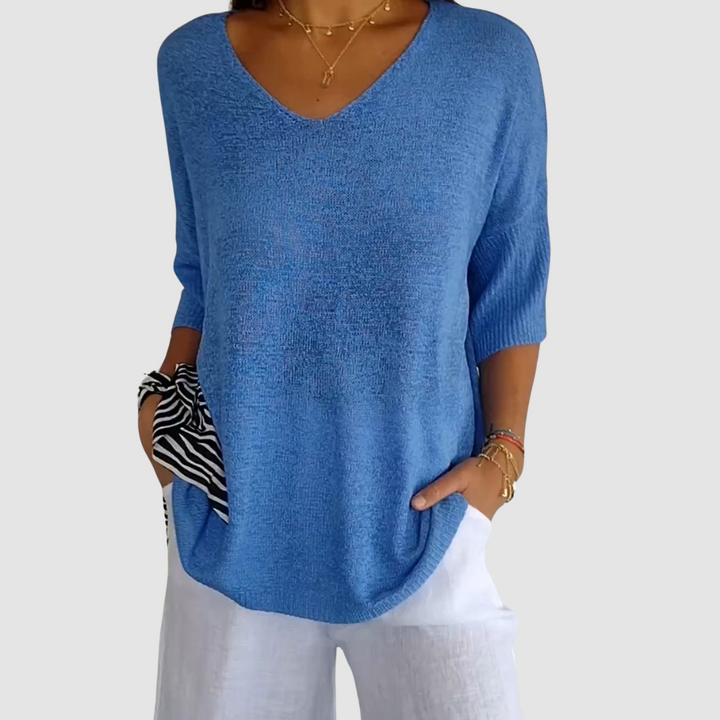 Blue knit V-neck top with short sleeves, worn with white pants. Model&