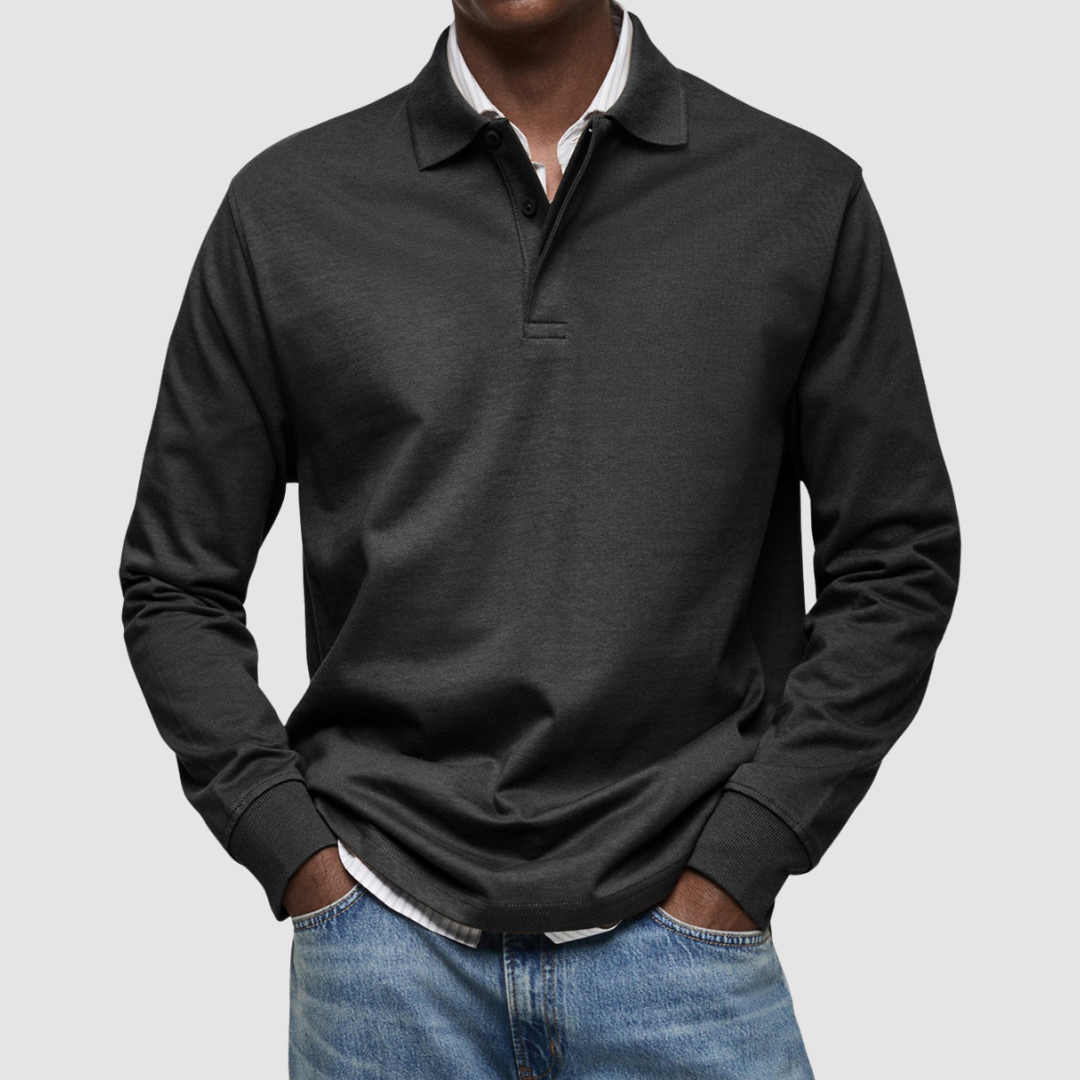 Black long sleeve polo shirt with button collar, worn over striped shirt, paired with jeans; studio setting.