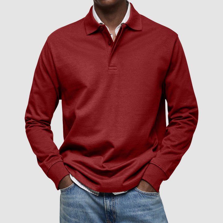Red long sleeve polo shirt with button collar, worn over striped shirt, paired with jeans; studio setting.