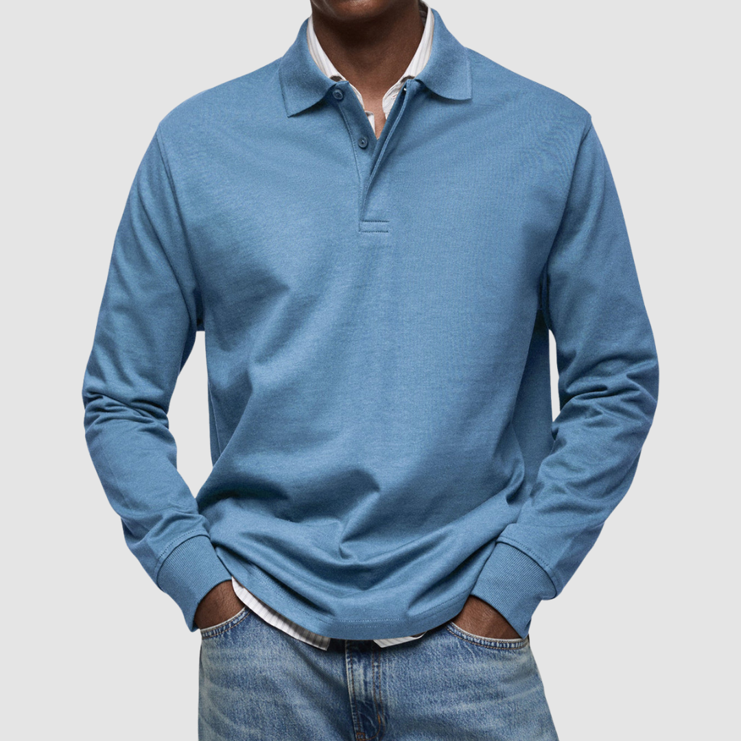 Blue long sleeve polo shirt with button collar, worn over striped shirt, paired with jeans; studio setting.