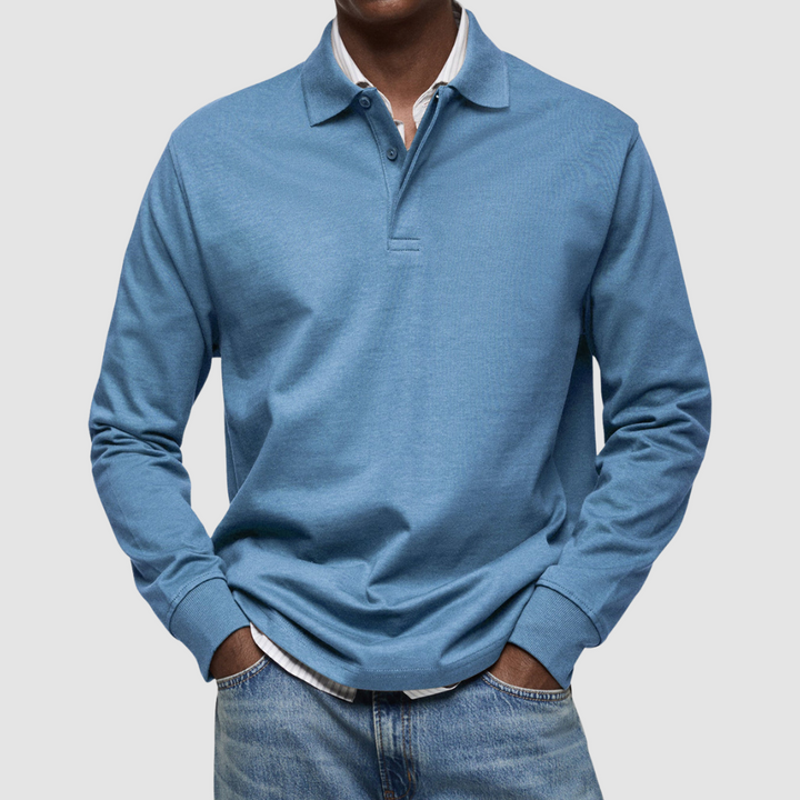 Blue long sleeve polo shirt with button collar, worn over striped shirt, paired with jeans; studio setting.