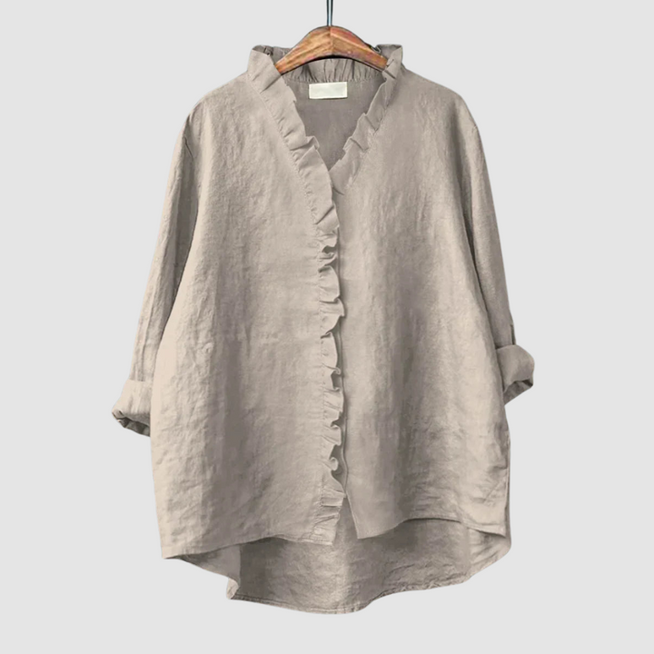 Neutral beige blouse with ruffled collar and button closure on wooden hanger, set against a light gray background.