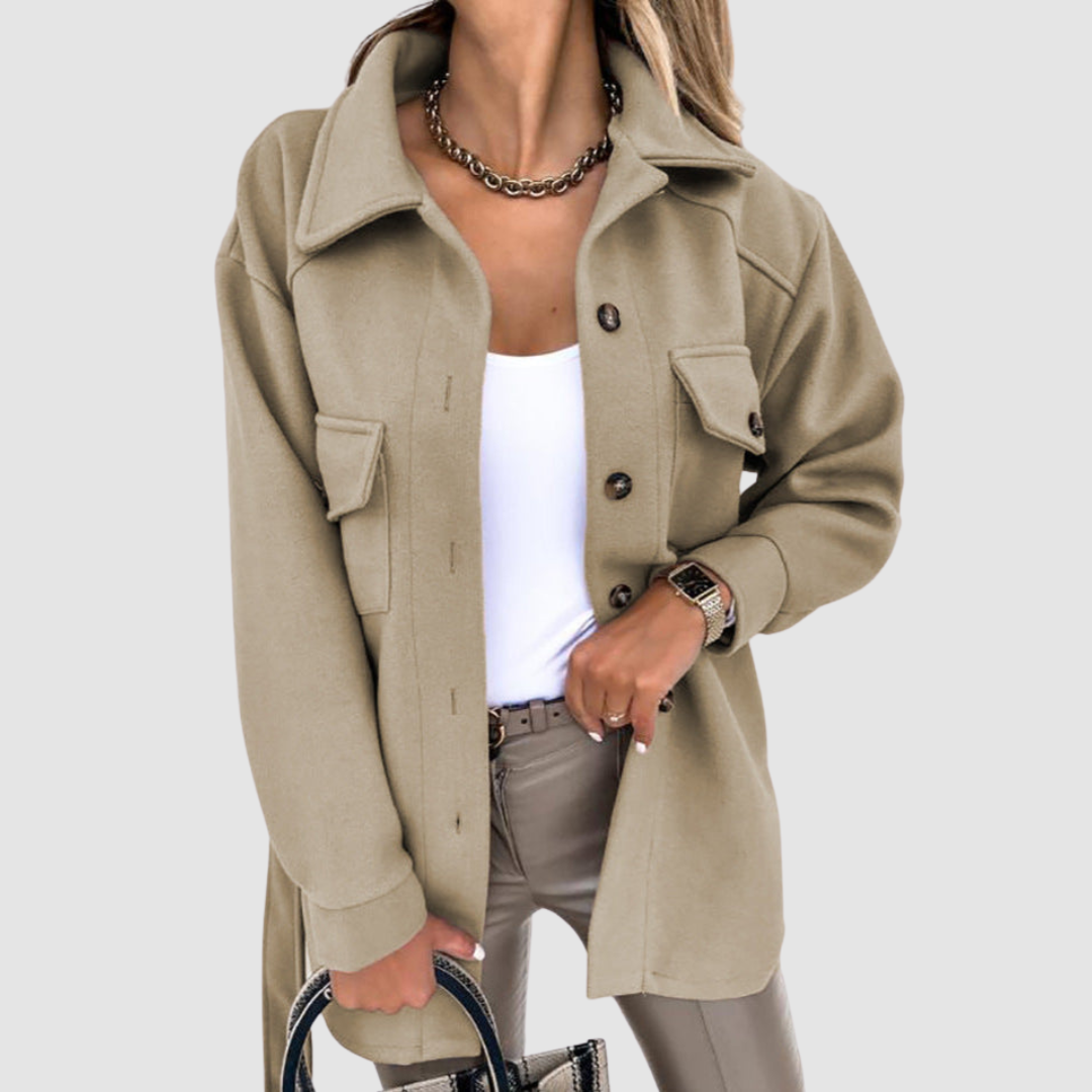 Chic woman wearing a light brown jacket with buttoned pockets over a white top on a gray backdrop.