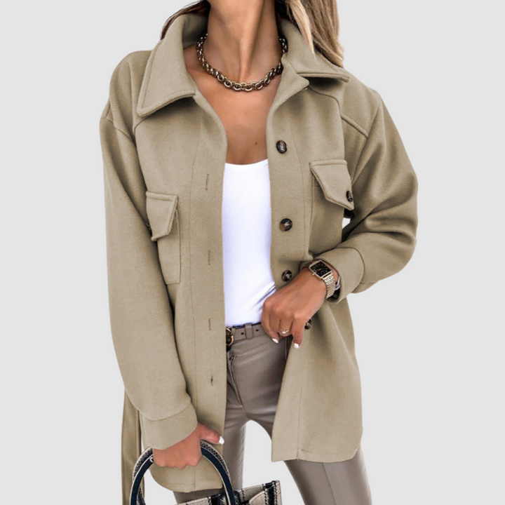 Chic woman wearing a light brown jacket with buttoned pockets over a white top on a gray backdrop.