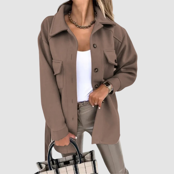 Fashionable woman in a taupe jacket with buttoned pockets, paired with a white top, set against a gray background.