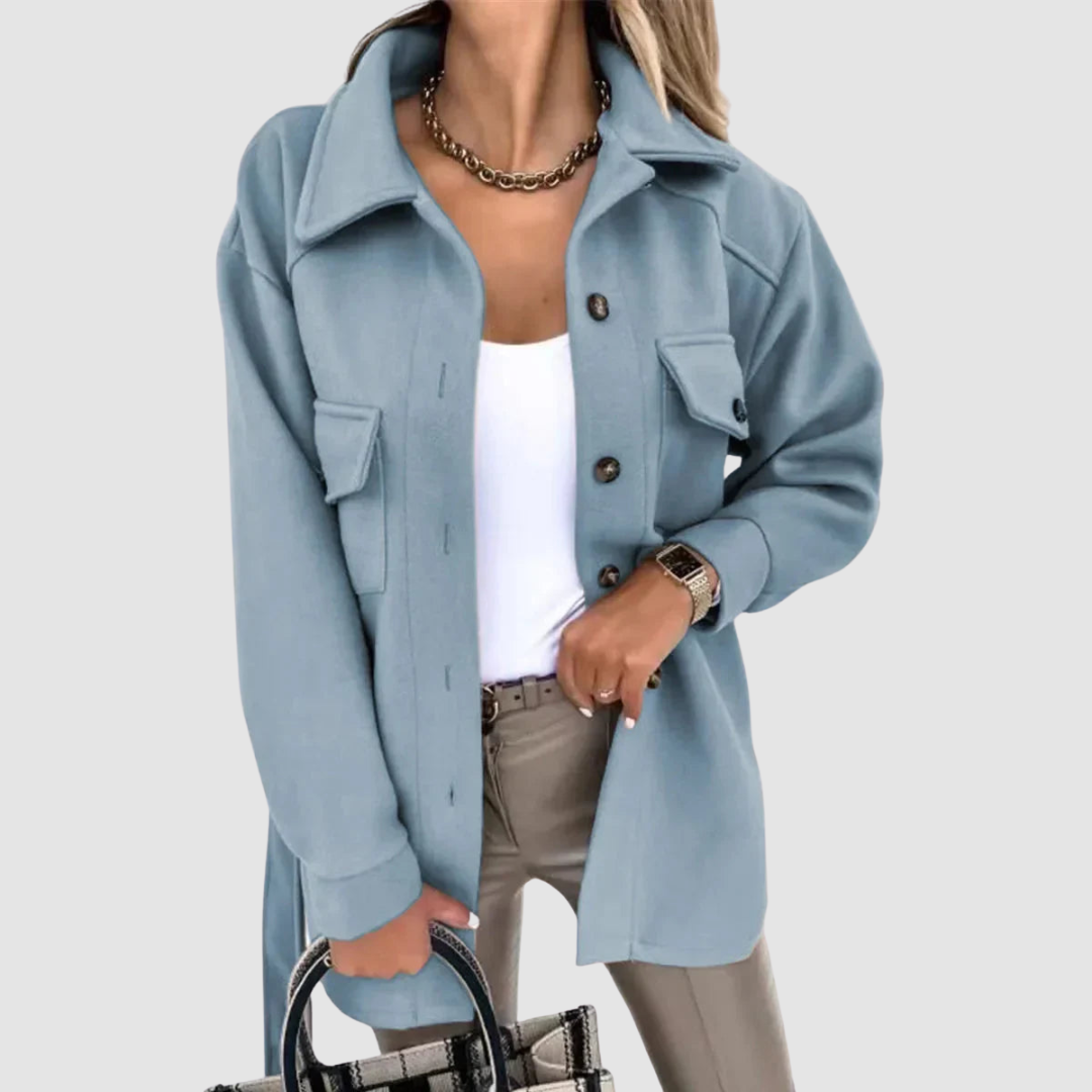 Elegant woman dressed in a light blue jacket featuring buttoned pockets and a white top on a light gray background.