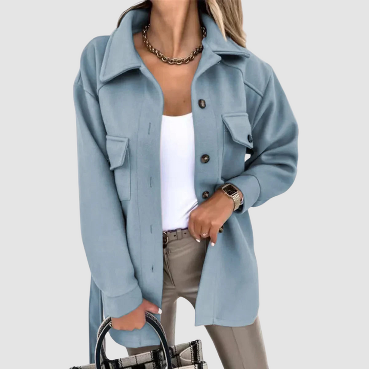 Elegant woman dressed in a light blue jacket featuring buttoned pockets and a white top on a light gray background.