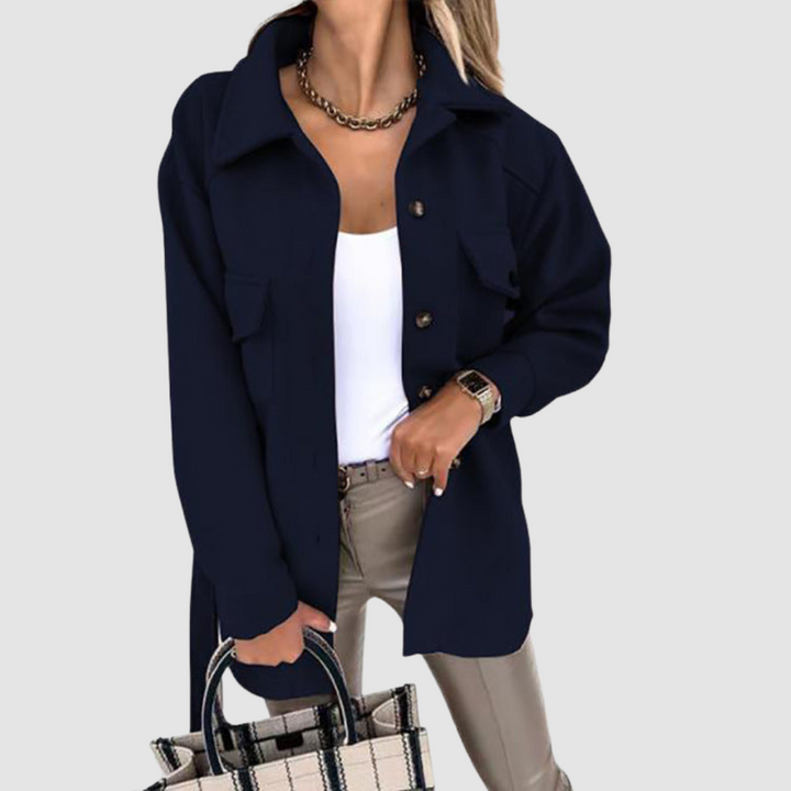 Trendy woman in a dark navy jacket with buttoned pockets over a white top, positioned on a gray background.