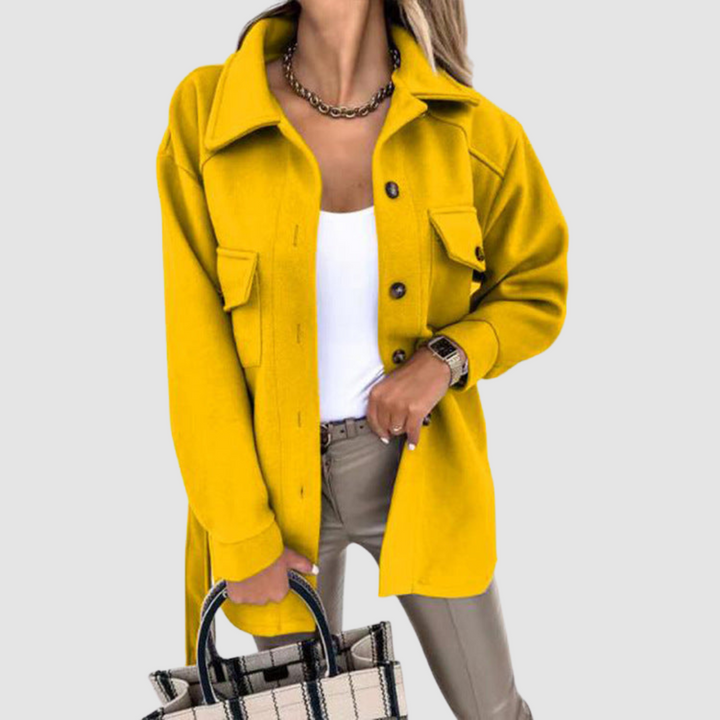 Vibrant woman wearing a yellow jacket with buttoned front pockets and a white top against a light gray background.