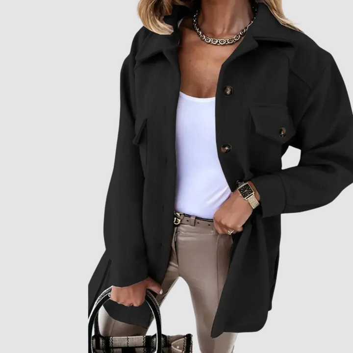 Sleek woman in a black jacket featuring buttoned pockets, complementing a white top, on a gray background.