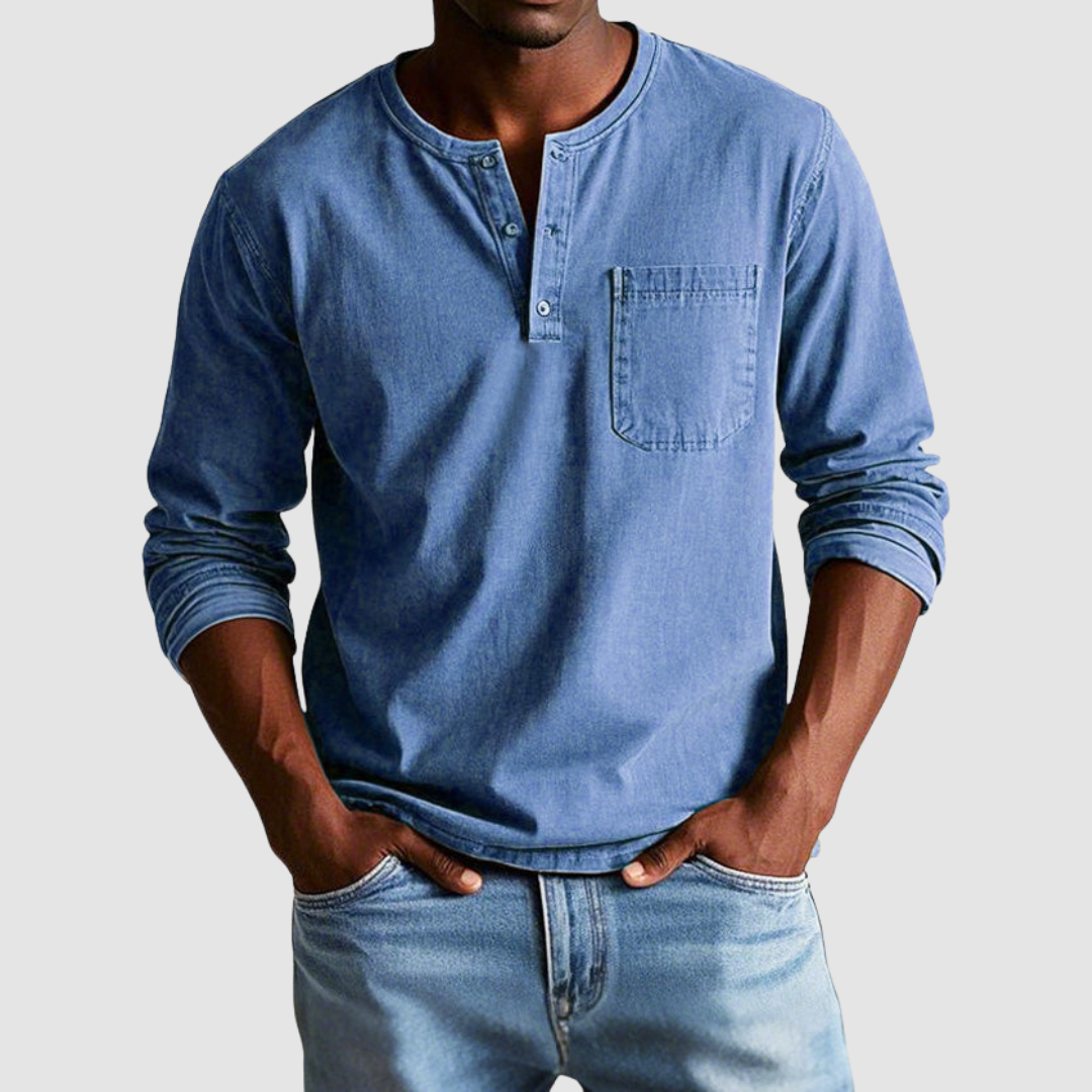 Man wearing a blue vintage Henley shirt, hands in pockets, in a studio setting against a light background.