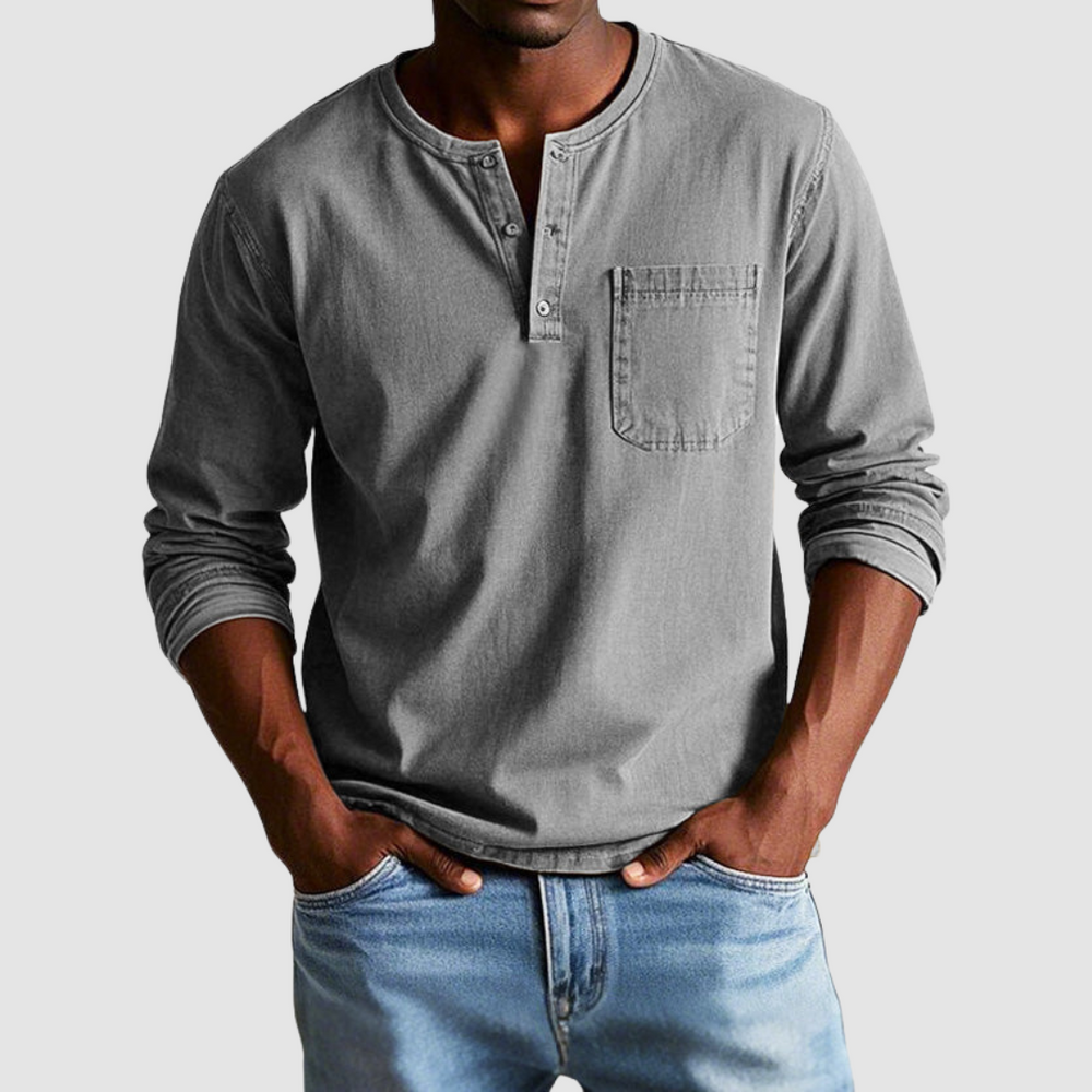 Man wearing a gray vintage Henley shirt, hands in pockets, in a studio setting against a light background.