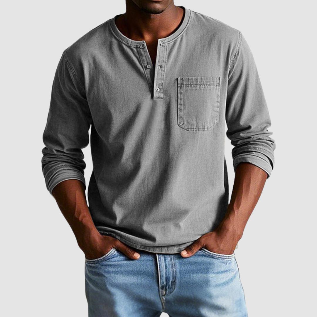 Man wearing a gray vintage Henley shirt, hands in pockets, in a studio setting against a light background.