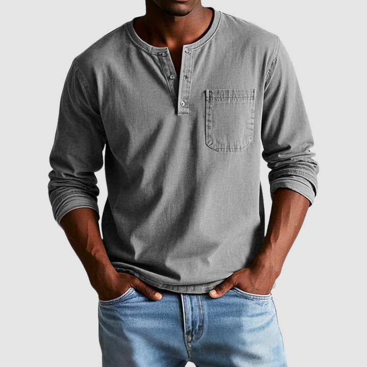 Man wearing a gray vintage Henley shirt, hands in pockets, in a studio setting against a light background.