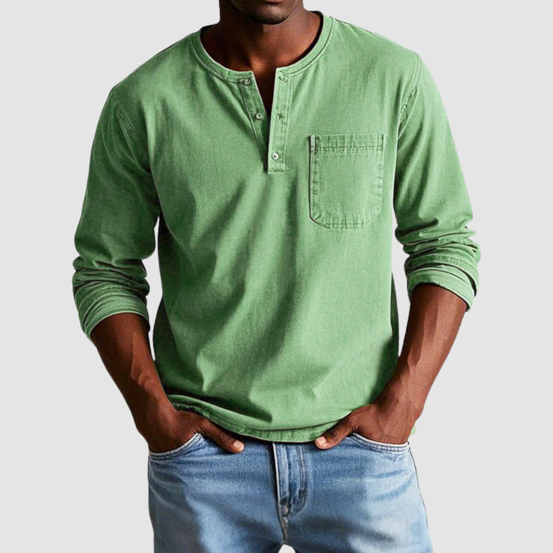 Man wearing a green vintage Henley shirt, hands in pockets, in a studio setting against a light background.