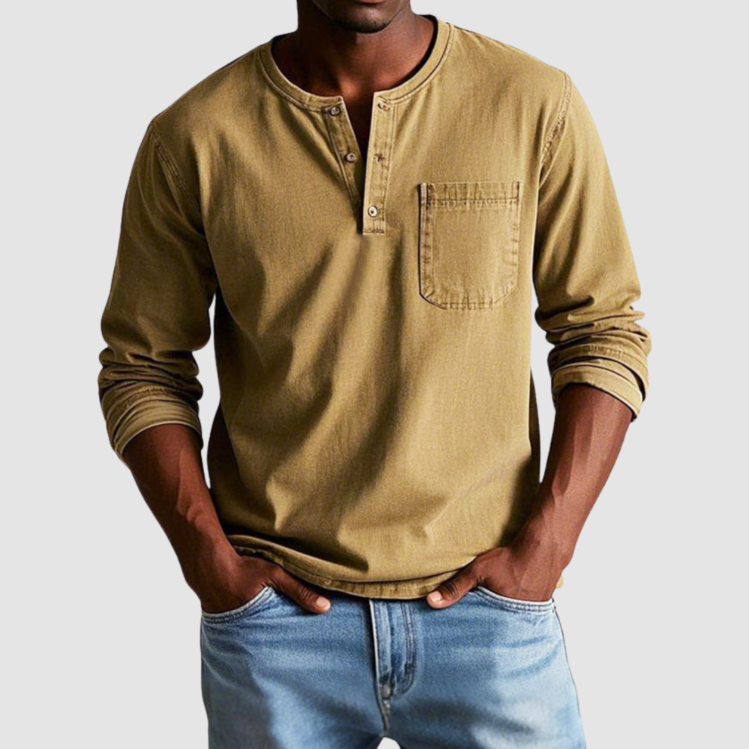 Man wearing a brown vintage Henley shirt, hands in pockets, in a studio setting against a light background.