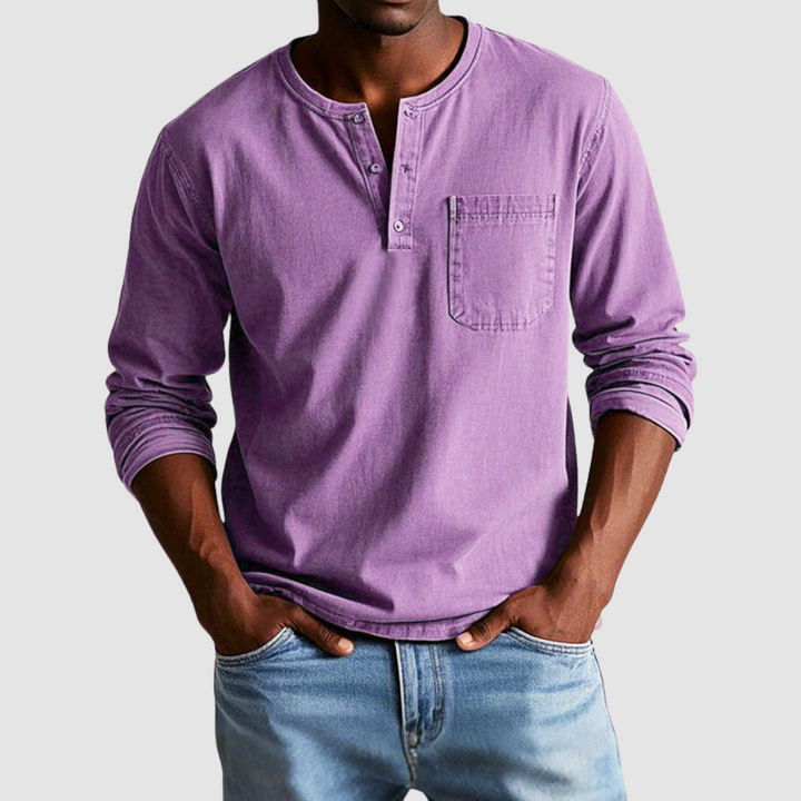Man wearing a purple vintage Henley shirt, hands in pockets, in a studio setting against a light background.