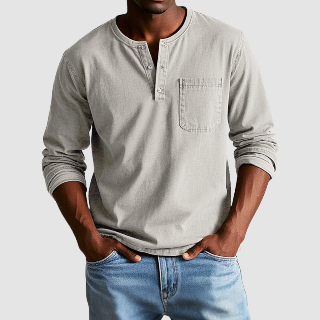 Man wearing a light gray vintage Henley shirt, hands in pockets, in a studio setting against a light background.