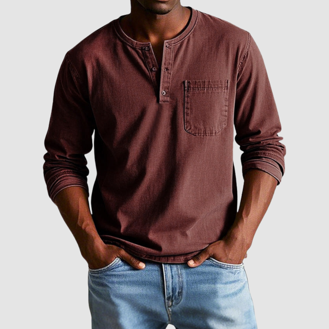 Man wearing a brown vintage Henley shirt, hands in pockets, in a studio setting against a light background.