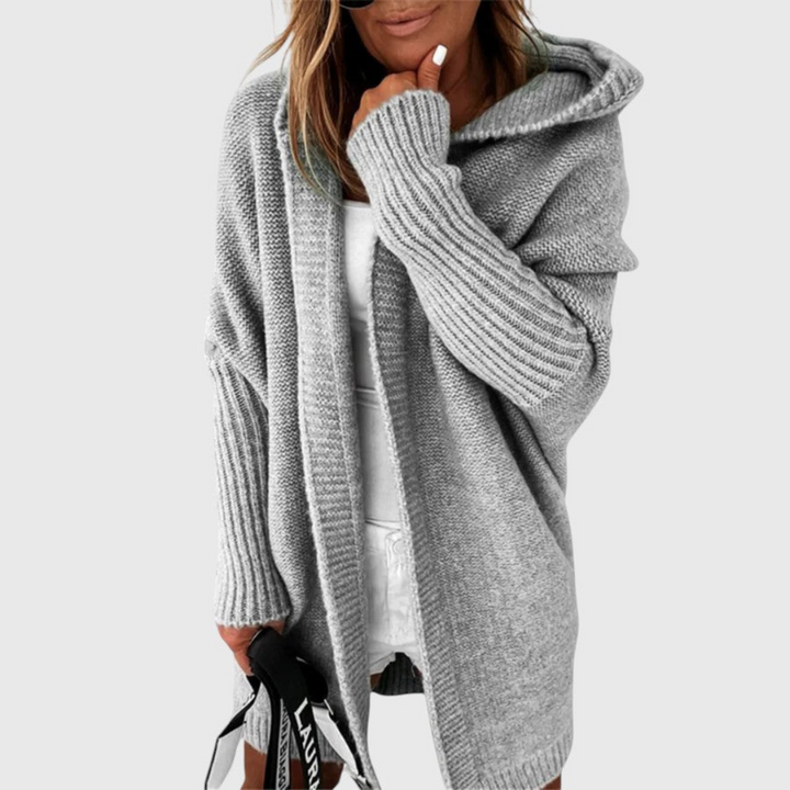 Gray cozy hooded cardigan worn by a person holding a bag, set against a plain background.