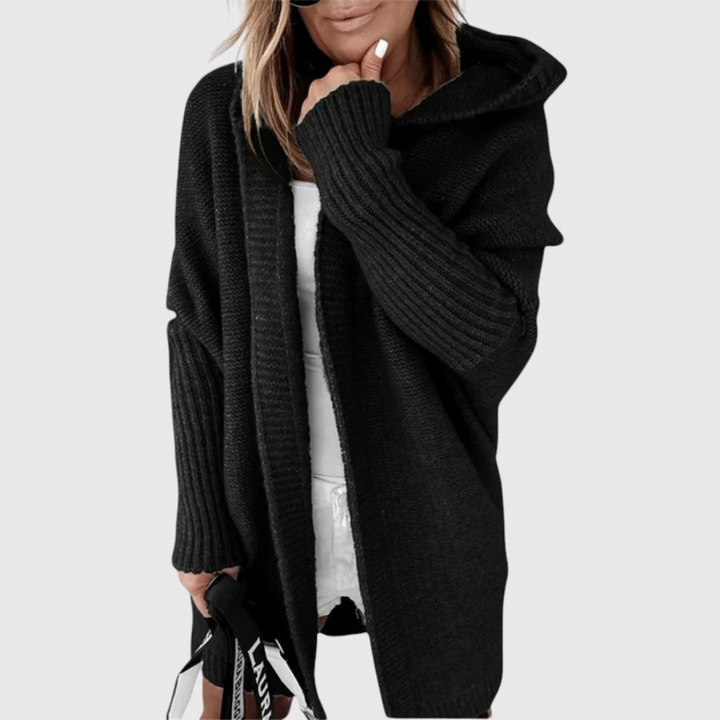 Black cozy hooded cardigan worn by a person holding a bag, set against a plain background.