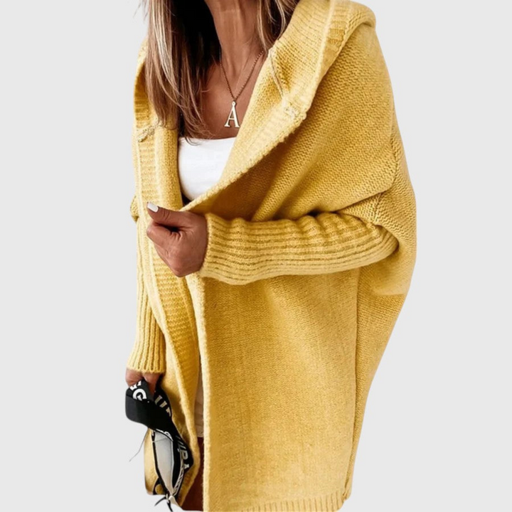 Yellow cozy hooded cardigan worn by a person holding a bag, set against a plain background.