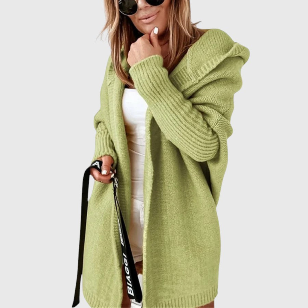 Green cozy hooded cardigan worn by a person holding a bag, set against a plain background.