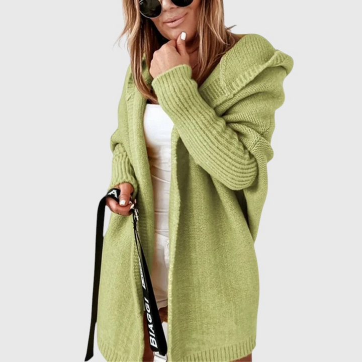 Green cozy hooded cardigan worn by a person holding a bag, set against a plain background.