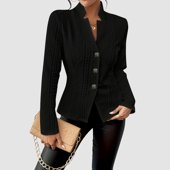 Black elegant blazer with textured patterns and button closure, styled with leather pants and a tan quilted clutch, studio backdrop.
