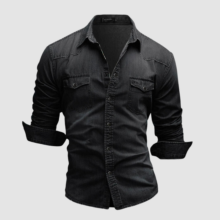 Black denim shirt with folded sleeves and button-up front displayed in a studio on a white background.
