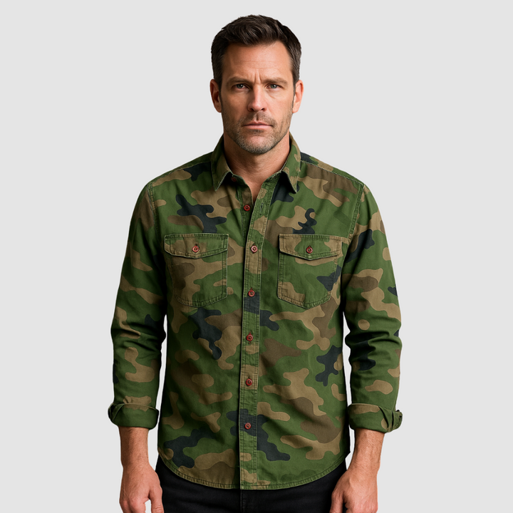 Man wearing a green urban camo shirt with rolled-up sleeves against a plain gray background.