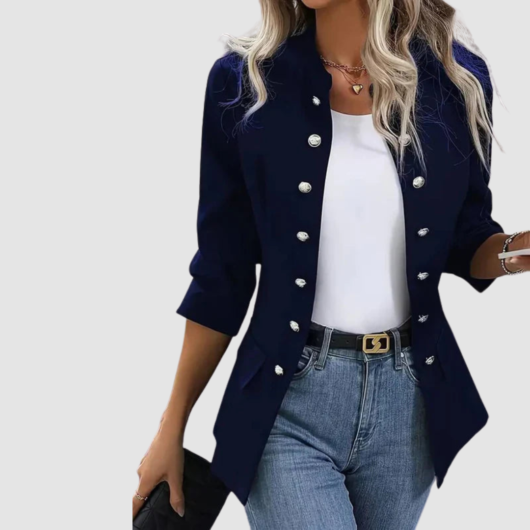 Model wearing a navy blazer with clasped buttons over a white top and jeans, styled with a belt, studio backdrop.