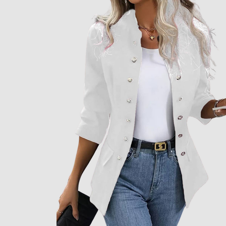White blazer with shiny buttons, worn over white top and jeans, complemented with black belt, studio setting.