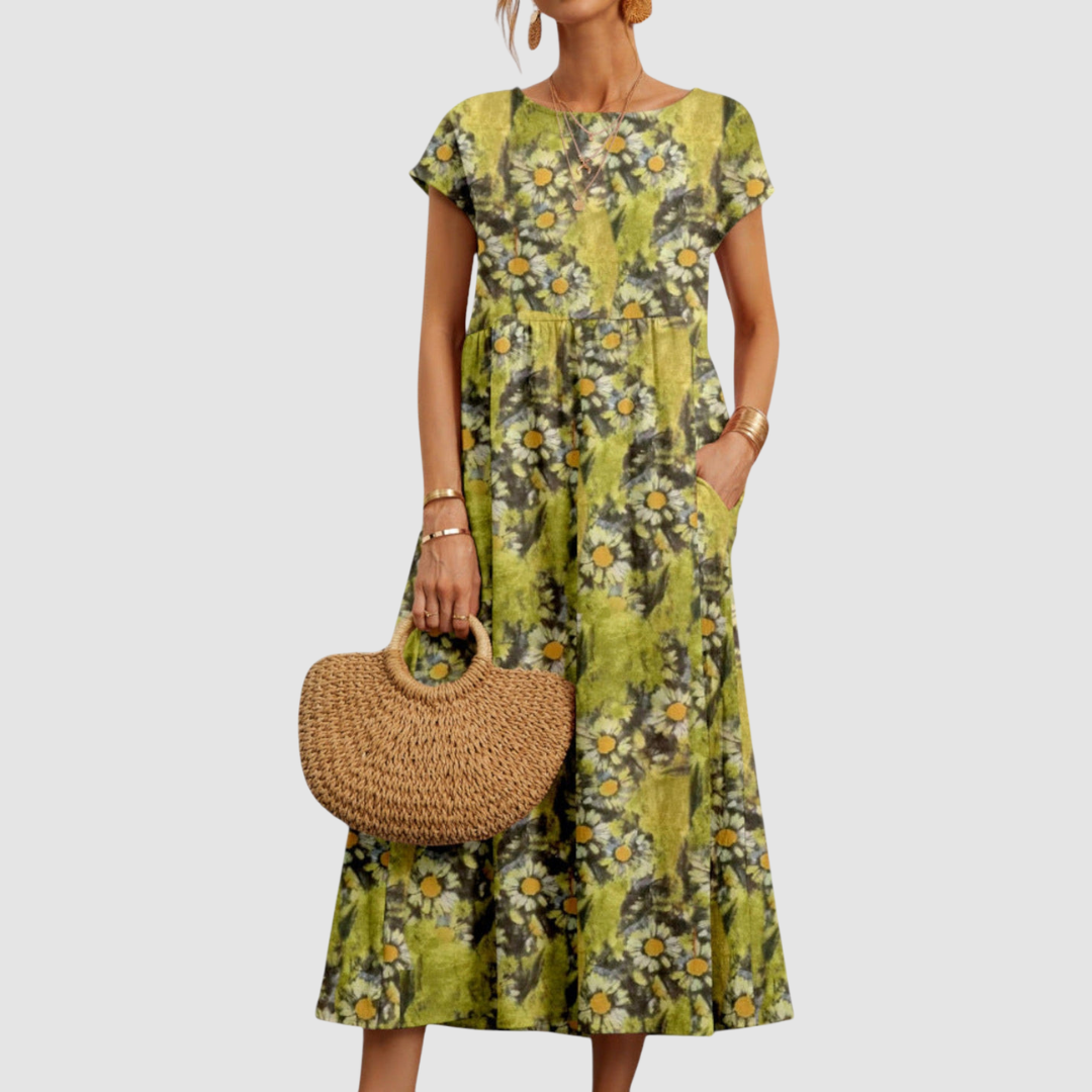 Green floral midi dress with short sleeves and yellow daisy pattern, styled with a straw tote, on a light gray background.