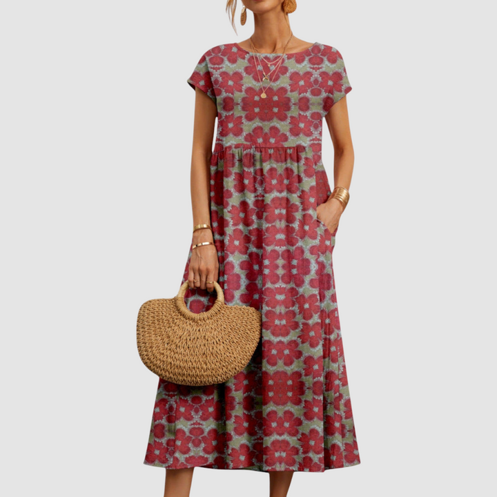 Red floral midi dress with short sleeves and round neckline, paired with a straw tote, against a light gray background.