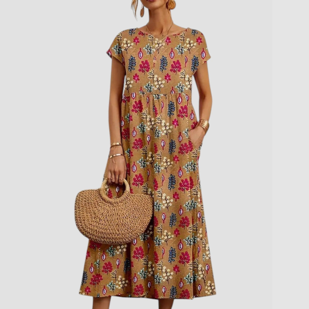 Beige midi dress adorned with pink and blue floral prints, short sleeves, paired with a straw tote, on a light gray background.