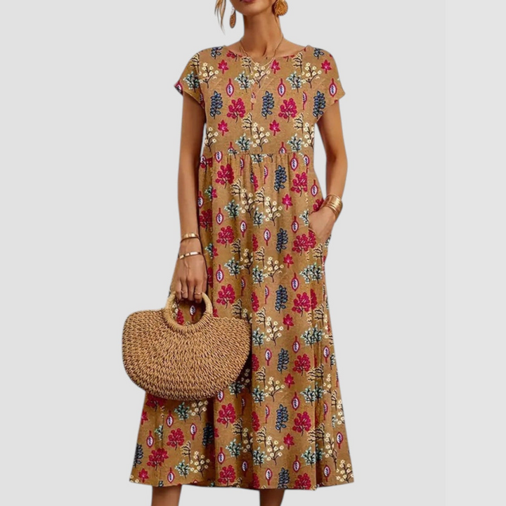 Beige midi dress adorned with pink and blue floral prints, short sleeves, paired with a straw tote, on a light gray background.