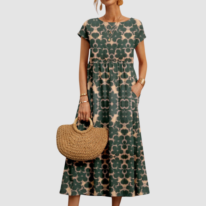 Dark green floral midi dress with beige patterns, featuring short sleeves and a straw handbag, set against a light gray backdrop.