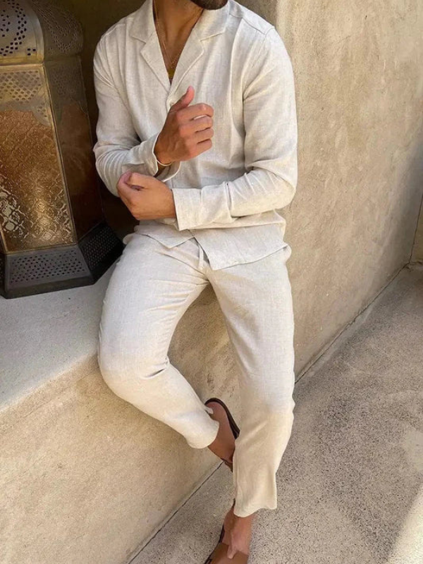 Beige summer set outfit with shirt and pants, modeled outdoors beside a decorative lantern on a stone bench.