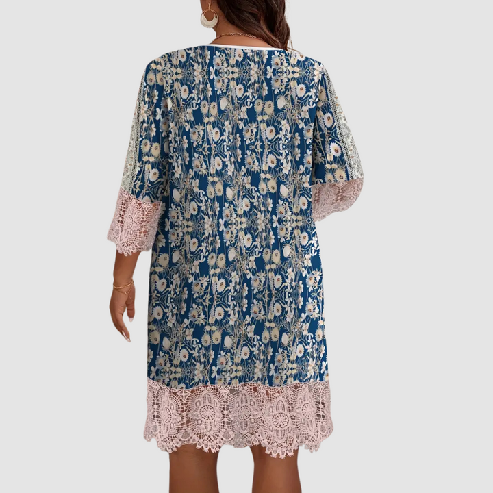 Back view of boho dress with blue and floral print, lace hem, worn by model against a plain background.