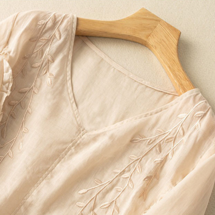 Close-up of cream fabric with detailed leaf embroidery, showcasing texture and elegant design.