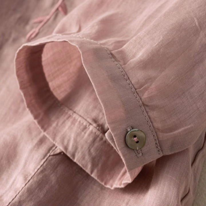 Close-up of mauve fabric with a buttoned sleeve, showcasing stitch details and button design.